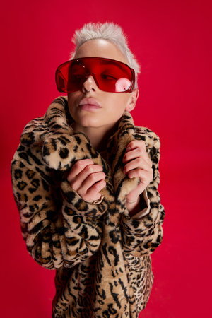 Portrait of young stylish woman with short hair posing in stylish coat with animal print isolated over red background. Autumn fashionの写真素材