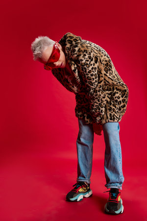 Portrait of young stylish woman with short hair posing in stylish coat with animal print isolated over red background. Youth styleの写真素材