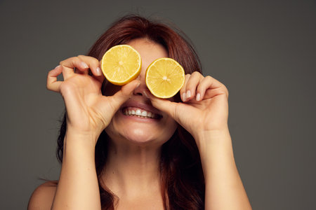 Portrait of beautiful red-haired woman, smiling, posing with lemons isolated over dark grey...