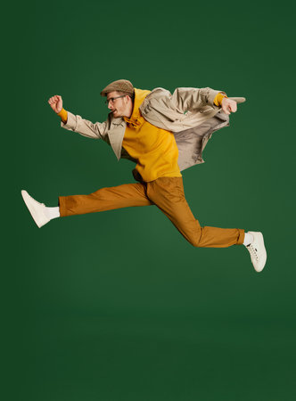Portrait of young stylish man in trendy clothes posing isolated over green background. In a hurry. Matching clothesの写真素材