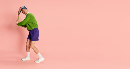 Portrait of young man in vintage sportive clothes posing with tennis racket isolated over pink background. Flyerの写真素材