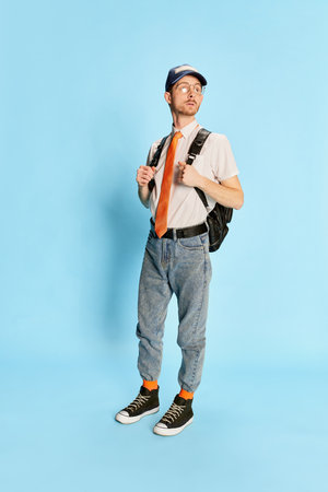 Portrait of young man, student in casual clothes posing isolated over blue background. First day at...