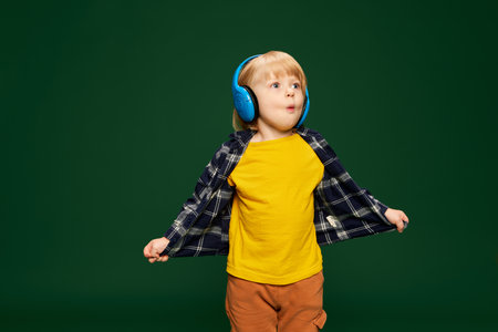 Portrait of little boy, child posing in headphones over green studio background. Interesting information. Concept of childhood, emotionsの写真素材