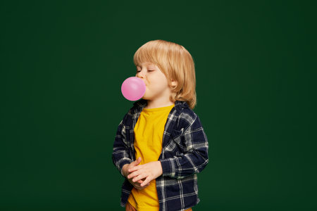 Portrait of little boy, child posing wit bubblegum over green studio background. Having fun. Concept of childhood, emotionsの写真素材