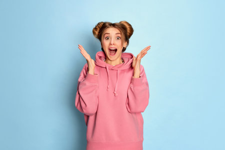 Portrait of young cute girl in pink hoodie posing with happy and excited face over blue studio background. Positivityの写真素材