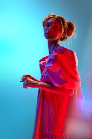 Portrait of young beautiful girl in white dress posing over blue background in neon lights....