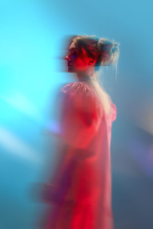 Portrait of young beautiful girl in white dress posing over blue background in neon lights. Unfocused effectの写真素材