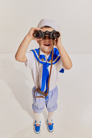 Portrait of little boy, child in image of seaman in vest posing with binoculars over grey background. Amazed travelerの写真素材