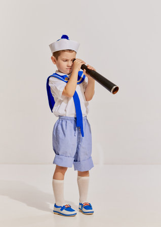Portrait of little boy, child in image of seaman in vest posing with spyglass over grey background. Curious kidの写真素材