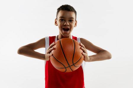 Portrait of boy in red uniform, basketball player posing with ball over grey studio background. Active lifestyleの写真素材
