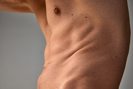 Cropped image of male body, belly over grey studio background. Body positivity. Low fat level....