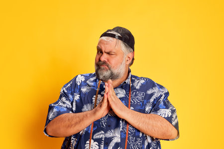 Portrait of fat mature man in stylish shirt posing with funny grimace face over bright yellow studio...