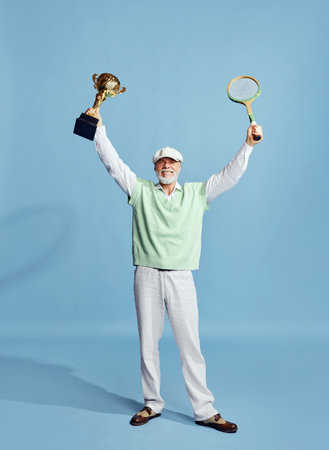 Winner. Portrait of handsome senior man in stylish outfit posing with tennis racket and trophy over...