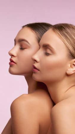 Blonde and brunette. Portrait of two young, beautiful girls with well-kept skin isolated over pink studio background. Concept of skincare, cosmetology, natural beautyの写真素材