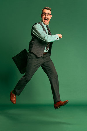 Happy worker. Portrait of handsome man, businessman in classical suit with briefcase over green studio background. Concept of emotions, occupation, lifestyleの写真素材