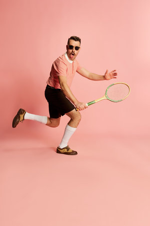 Portraits of handsome charismatic man in stylish clothes posing with tennis racket, playing over pink studio background. Concept of fashion, sport, lifestyleの写真素材