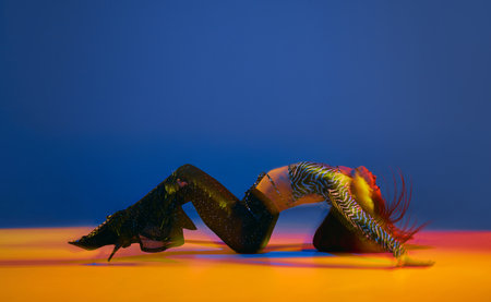 Portrait of young flexible girl dancing heels dance in stylish clothes over blue background in neon...