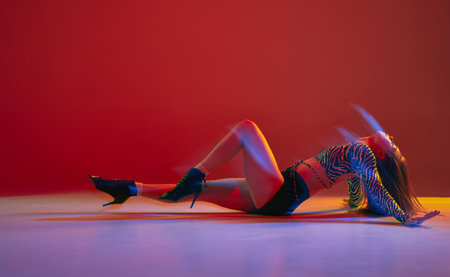 Passion, femininity. Portrait of young girl dancing heels dance over red background in neon with mixed light. Concept of modern dance styleの写真素材