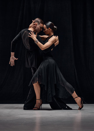 Passion, romance, emotions. Man and woman, professional tango dancers performing in black stage costumes over black background.の写真素材