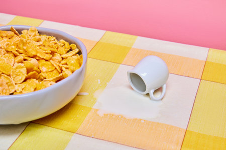 Food pop art photography. Bowl with cereal, corn flakes on yellow tablecloths with milk jar and spilled milk. Breakfast timeの写真素材