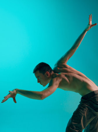Contemporary dance style. Young shirtless, muscular man dancing over blue, cyan studio background. Well-coordinated movementsの写真素材