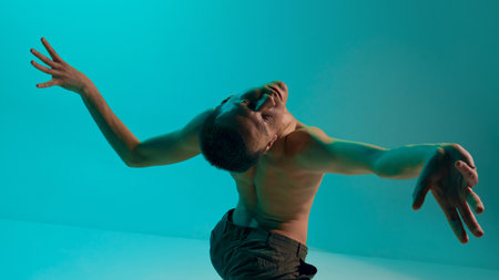 Bottom view. Contemporary dance style. Young expressive, flexible, shirtless man dancing over blue,...