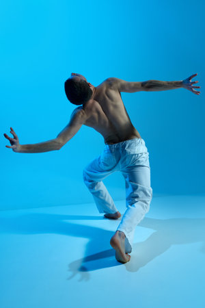 Contemporary dance style. Young artistic man dancing contemp, experimental dance over blue studio background. Beauty of movementsの写真素材