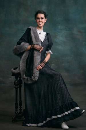Beautiful woman in image of Anna Karenina in stylish dark dress posing over vintage dark green...