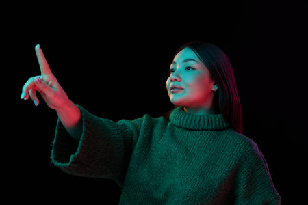 Modern technologies. Young brunette girl in cozy sweater working with digital screen over dark...