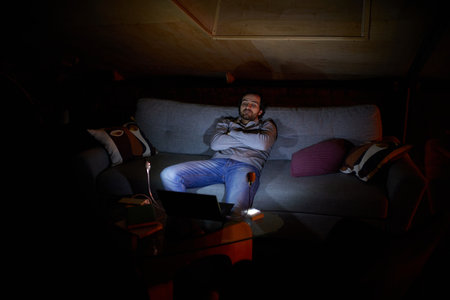 Power bank lamp light. Coziness. Young man sitting together on couch at home in the evening and watching movie on laptop. No electricity, blackoutの写真素材