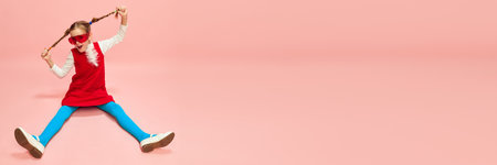 Cute little girl, child with two pigtails posing in red dress and blue tights over pink studio background. Concept of emotions, childhoodの写真素材