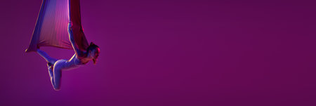 Flying. Young flexible girl doing aerial yoga, training over purple studio background in neon light. Concept of fitness and healthy lifestyle. Bannerの写真素材