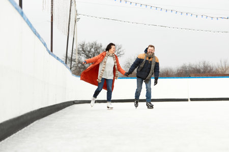Happiness, positive mood. Middle-aged couple skating on open air ice rink in warm winter day....