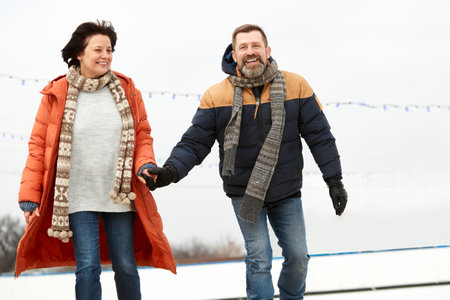 Middle-aged smiling happy people, man and woman spending time on open ice rink in winter day. Concept of leisure activity, winter hobby, relationship, emotionsの写真素材