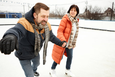Middle-aged couple, man and woman having fun outdoors, skating on open air ice rink in winter day. Concept of leisure activity, winter hobby, relationship, emotionsの写真素材
