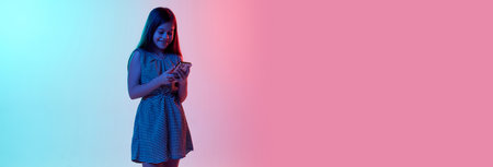 Online communication. Little smiling girl, child chatting on phone over gradient blue pink studio...