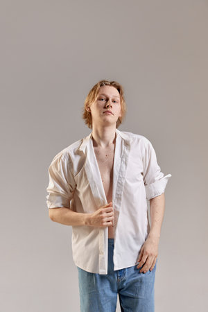 Wellbeing, self-acceptance. Portrait of young redhead woman posing in white shirt and jeans over...