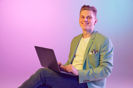 Happy. Freelance, influencer. Young handsome man in stylish jacket posing, working on laptop over...