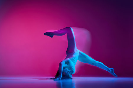 Dynamic portrait of young flexible woman dancing contemp, freestyle dance over gradient pink studio background in neon with mixed lights. Concept of dance aesthetics, artの写真素材