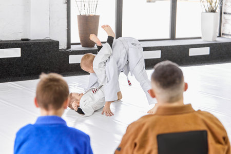 Kids training judo, jiu jitsu, practising exercises in front of coach and pupils. Children learning indoorsの素材 [FY310198979189]