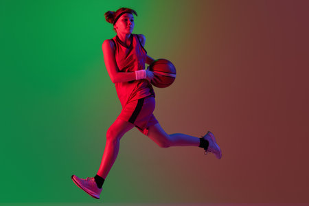 Active player in motion. Teen girl, basketball player isolated over gradient green red background in neon light. Concept of professional sport and hobbyの写真素材