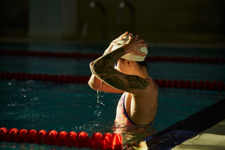 Preparing to swim. Young woman, professional female swimming athlete in cap and goggles posing in pool indoor. Concept of sport, endurance, competitionの写真素材