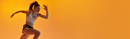 Dynamic image of young sportive girl, professional runner training over orange studio background in neon light. Concept of sport. health and strengthの写真素材