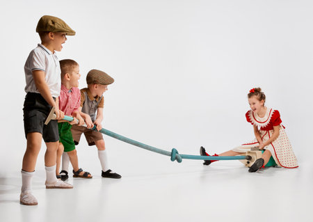 Children, boys and girls in stylish retro clothes playing with vacuum cleaner against grey studio...