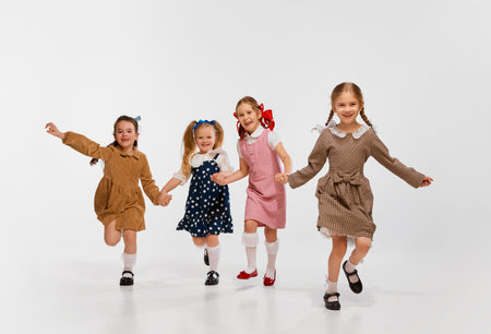 Four beautiful little girls, kids in stylish retro dresses posing, running against grey studio background. Concept of childhoodの写真素材