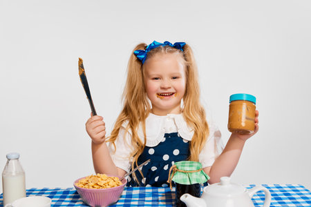 Happy smiling little girl, kid eating, having delicious breakfast against grey studio background. Concept of childhoodの写真素材