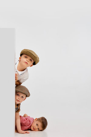Three little kids, boys peeking out corner, playing against grey studio background. Concept of childhoodの写真素材