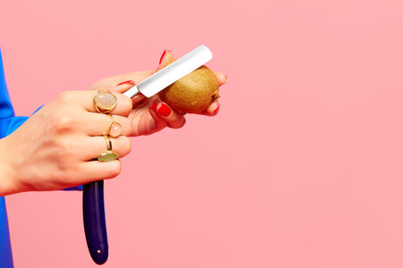 Female hand peeling kiwi with razor against pink studio background. Food pop art photography. Creativity and artの写真素材