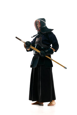 Portrait of man, professional kendo athlete in uniform posing with shinai sword against white studio...