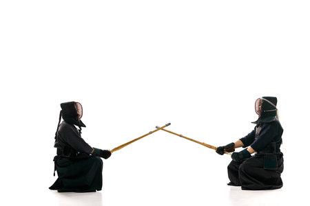 Start of fight. Two men, professional kendo athletes in uniform with helmet with bamboo shinai sword against white studio backgroundの写真素材